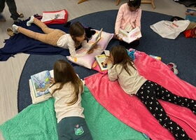 Kinder liegen auf Decken und lesen in Büchern