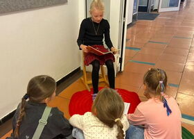 Eine Schülerin sitzt auf einem Stuhl und liest anderen Schülerinnen daraus vor