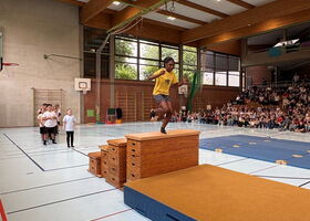Eine Schülerin springt in der Turnhalle von einem Kastensportgerät auf eine Matte