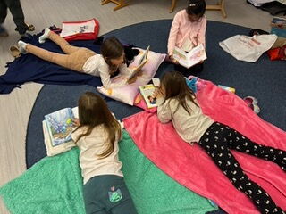 Kinder liegen auf Decken und lesen in Büchern