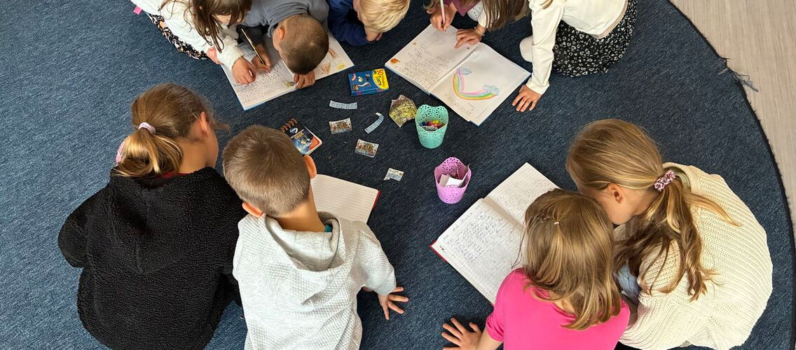 Kinder sitzen gemeinsam auf einem Teppich und nehmen Hefteinträge vor