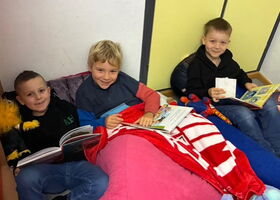 Drei fröhliche Schüler sitzen mit je einem Buch auf bequemen Sitzmöglichkeiten