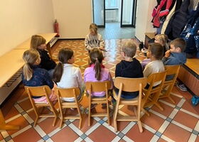 Eine Schülerin liest Schülern im Stuhlkreis aus einem Buch vor