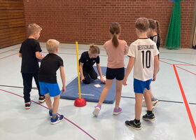 Schulkinder mit einer Trainerin an einer Matte in der Turnhalle